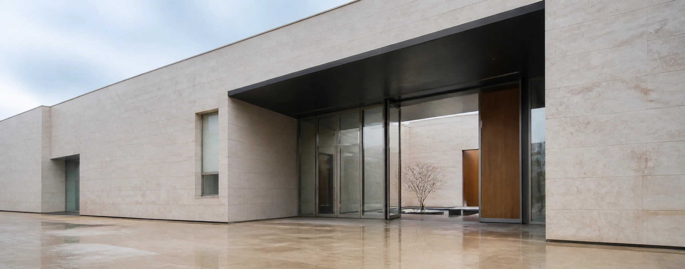 Entrada arquitectónica de piedra, vidrio y metal con luz natural neutra